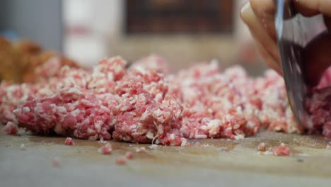 close up of hands using a knife to mince ground meat for a meal preparation