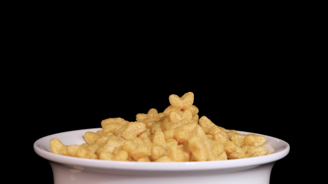 Cereal pieces fall into a white bowl against a black background, captured in slow motion for a dynamic visual effect