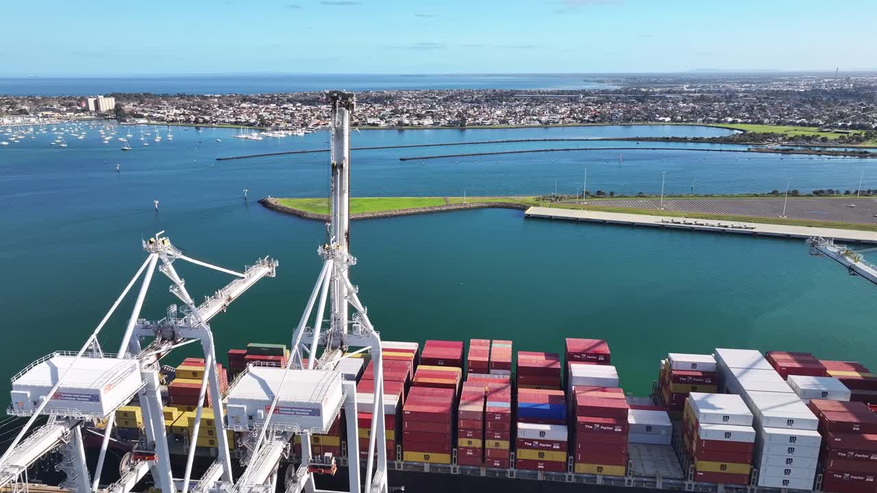 Cargo vessels docked beside cranes at Melbourne container terminal overlooking Port Phillip Bay