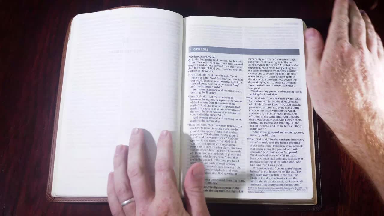 Top down shot opening up a leather bound bible to the book of Genesis on a wooden table