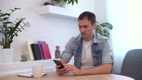 Professional-Creative-Man-Sitting-at-His-Desk-in-Home-Office,-Using-Smartphone,-Man-Using-Mobile-Phone,-Browsing-Through-Internet,-Social-Networks,-Media.