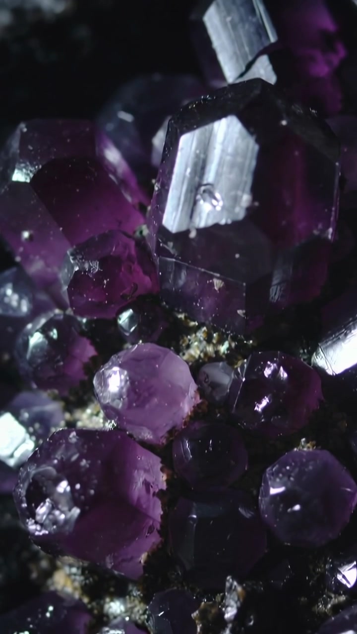 Vidéo verticale : La caméra se déplace pour un gros plan macro sur un amas de prismes violets, révélant des éclats.