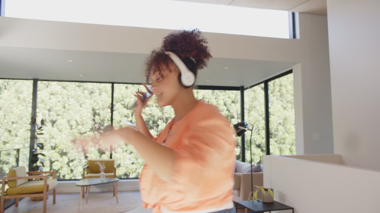 Dancing and enjoying music, woman wearing headphones and holding smartphone indoors