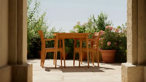 outdoor patio with wooden table and chairs surrounded by lush plants