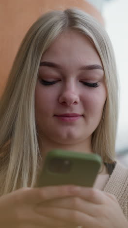 primer plano de una joven que opera un iphone con caja verde mientras está sentada en una mesa de madera. sus manos están enfocadas en la pantalla, mostrando atención a los detalles en un entorno relajado