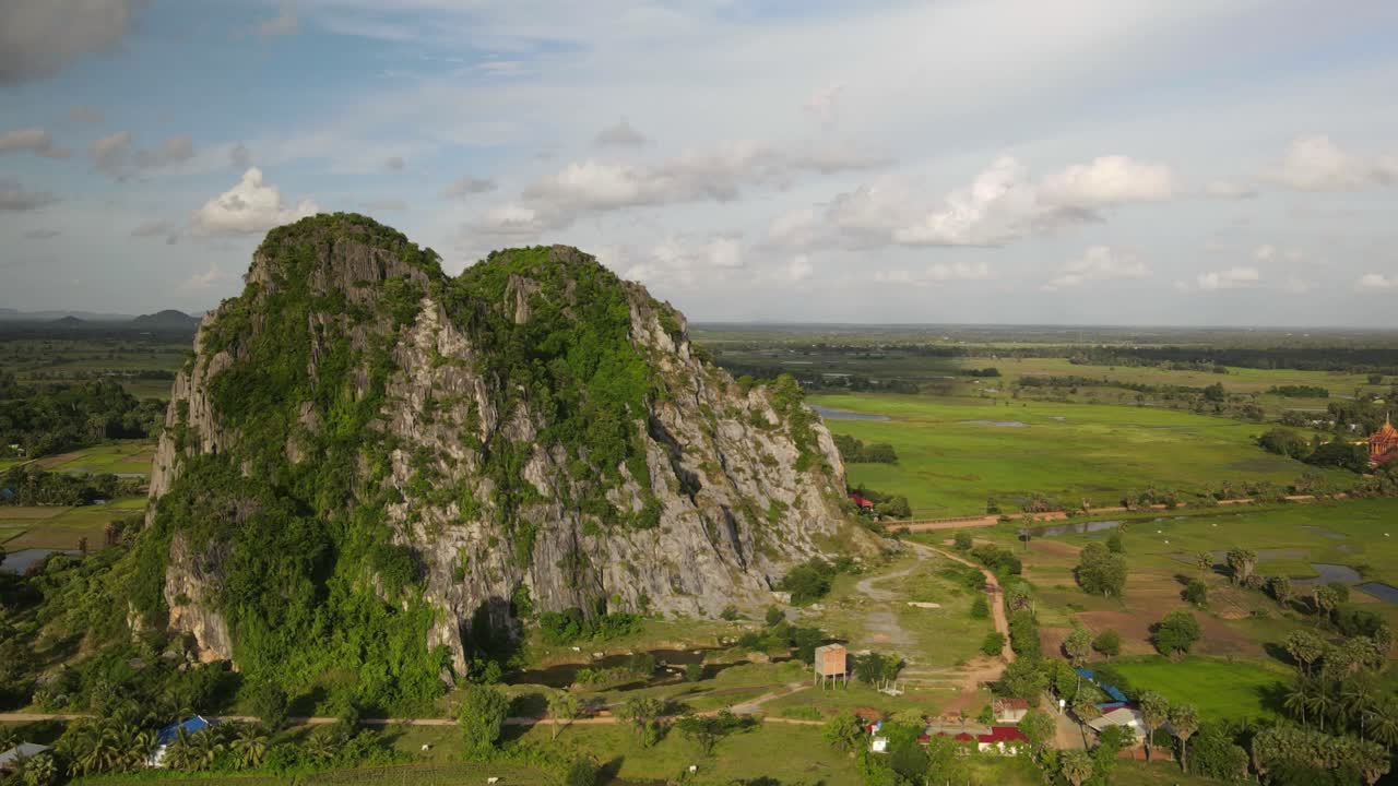 Lime stone formations protrude on the flat vivid green paddy planes of Cambodia.  Kampong Track, a protected area from the cement industry.  Drone aerial Time lapse of passing clouds.