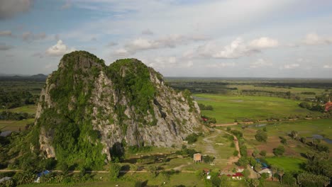 lime stone formations protrude on the flat vivid green paddy planes of cambodia.  kampong track, a protected area from the cement industry.  drone aerial time lapse of passing clouds.