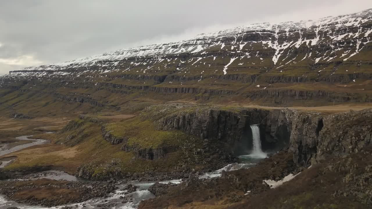 una cascada que desemboca en un exuberante valle cubierto de nieve en islandia