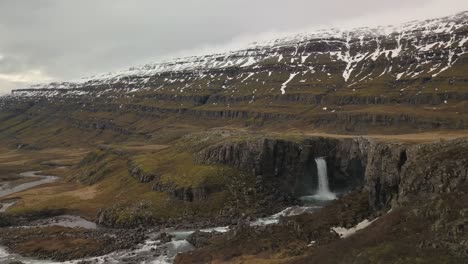 waterfall pouring into lush snow capped valley in iceland