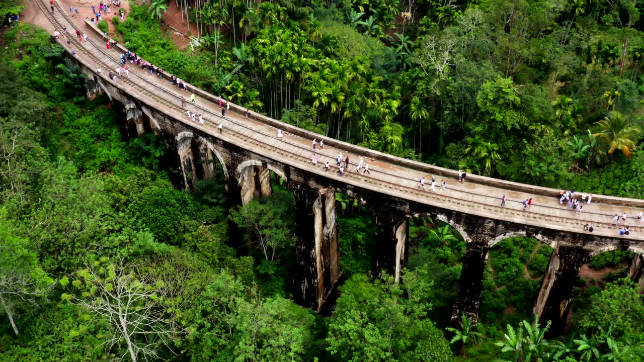 Drone flies above the Nine Arches Bridge in Ella, Sri Lanka, showing the structure surrounded by lush green trees from a top-down view