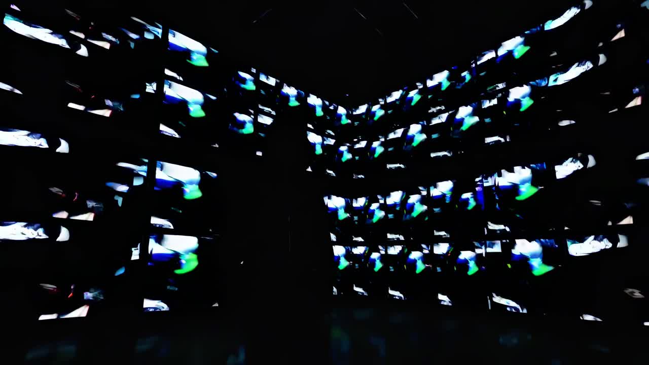 A person silhouetted against a wall of colorful video screens