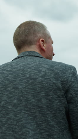 a close-up body view of an aged man wearing a gray jacket, seen from behind, with a sky in view