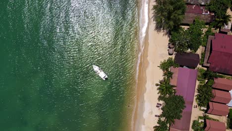 Tropeninsel-Drohne,-Vogelperspektive-Mit-üppig-Grünem-Regenwald-Und-Tropischen-Palmen-Mit-Kleinem-Bungalow-Resort-An-Einem-Weißen-Sandstrand-Mit-Schnellboot-Im-Wasser