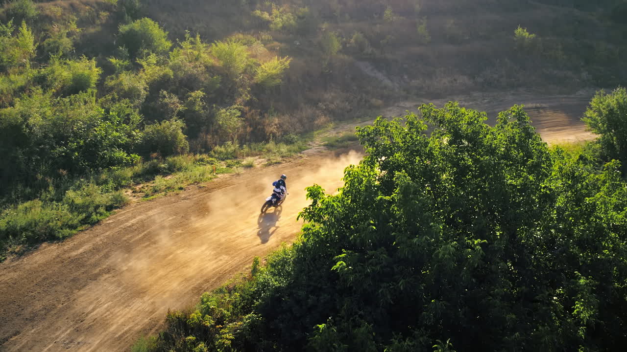 Ripresa aerea con drone di motociclisti che saltano da trampolini durante una gara di motocross, pista fangosa, moto da rally, vegetazione circostante. Rallentatore