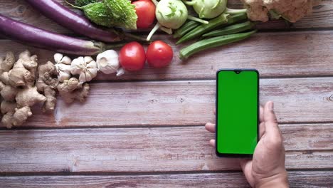 verduras frescas y teléfono de la tienda con pantalla verde en la mesa