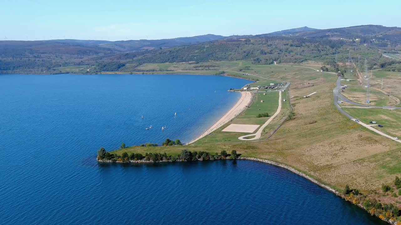 사람들이 일광욕과 목욕을 하는 호수 해변, 작은 범선 항해, 정원, 배경에 있는 집들이 있는 산책로