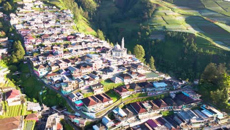 Aerial-view-of-beautiful-cit-located-on-slope-with-Mosque-during-sunny-day---Plantation-fields-with-growing-vegetables