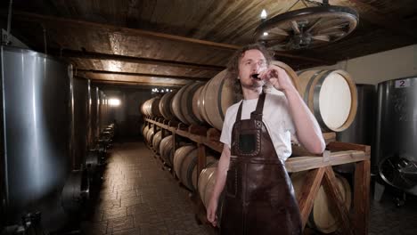 authentic shot of successful male sommelier is tasting a flavor and checking white wine quality poured in transparent glass in a wine cellar.