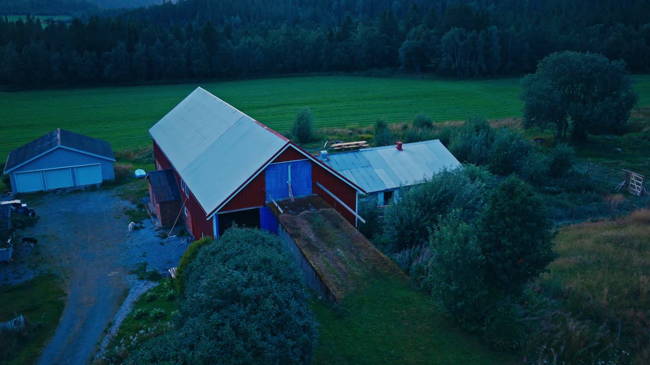 Flygfoto över en röd lada och jordbruksbyggnader i ett lantligt landskap.