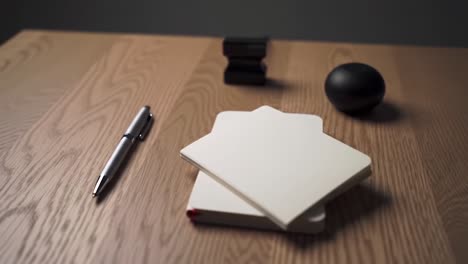 a serene workspace scene featuring notebooks, a pen, a paper clip holder, and a smooth black sphere, capturing a moment of creativity and organization