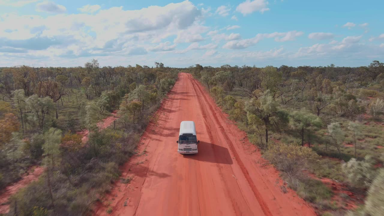 disparo de avión no tripulado, un autobús camper conduciendo a lo largo del camino de arena roja del interior en el desierto australiano
