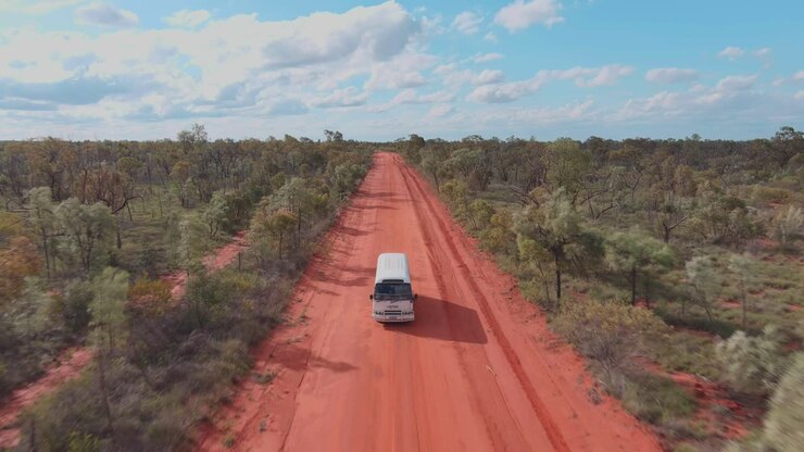 Drone shot, A camper bus driving along the red sandy road of the outback in the Australian desert