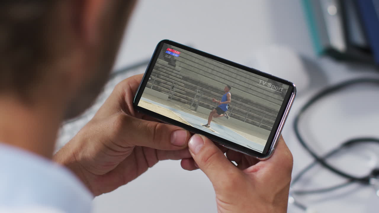 compuesto de un médico masculino viendo un evento de salto de longitud de atletismo en un smartphone