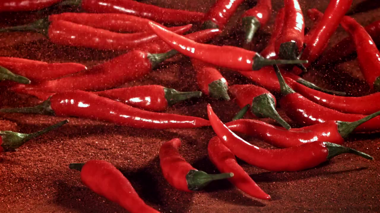 Red Chili Peppers Falling onto Chili Powder in Slow Motion