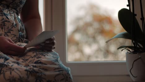 memories-a-young-girl-is-sitting-by-the-window-holding-a-picture-looking-at-her