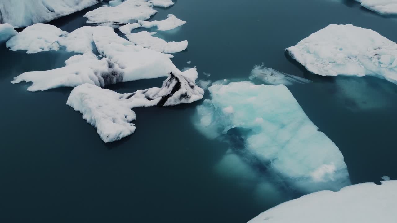Beatiful black and white icebergs floating in a lagoon in Iceland disappear into the blue water