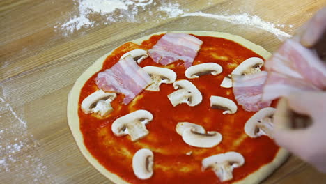 putting mushrooms and bakon on pizza dough with tomato souce. food video footage. hands of a chef with ingredients for pizza.