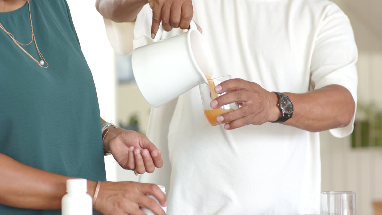 African American couple pouring white jug into glass, opening pill bottle kitchen counter for meds