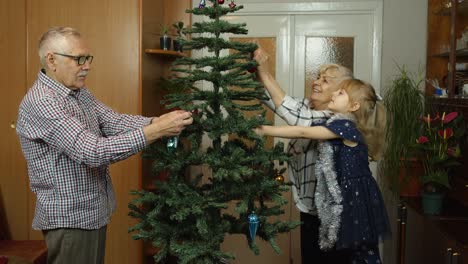 niña linda con abuelos mayores familia decorando árbol de navidad artificial en casa