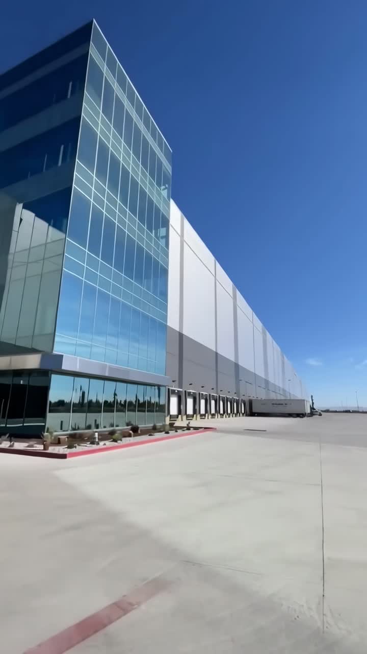 Vídeo a ángulo bajo de un edificio industrial moderno con fachada de cristal bajo un cielo azul despejado