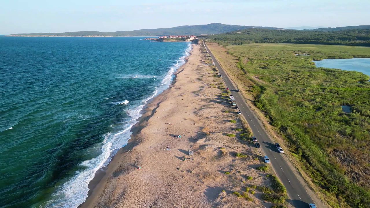 Вид с дрона на длинное песчаное побережье рядом с водно-болотными угодьями и бирюзовым морем в Италии. Параллельная прибрежная дорога простирается между водой и зеленым ландшафтом.