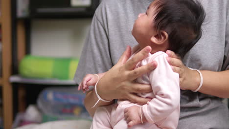 tapping the back of a newborn infant, the mother is helping her child to burp to release some gas after having its meal