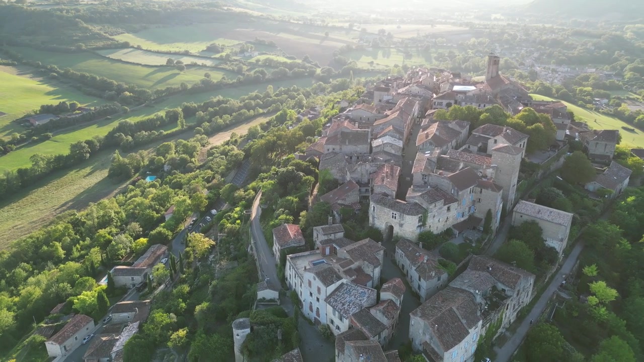 Vista aerea con drone nella campagna francese di una piccola e antica città medievale in mattoni su una cima di montagna, circondata da campi verdi, con volo all'indietro in una giornata di sole a Cordes-sur-Ciel.