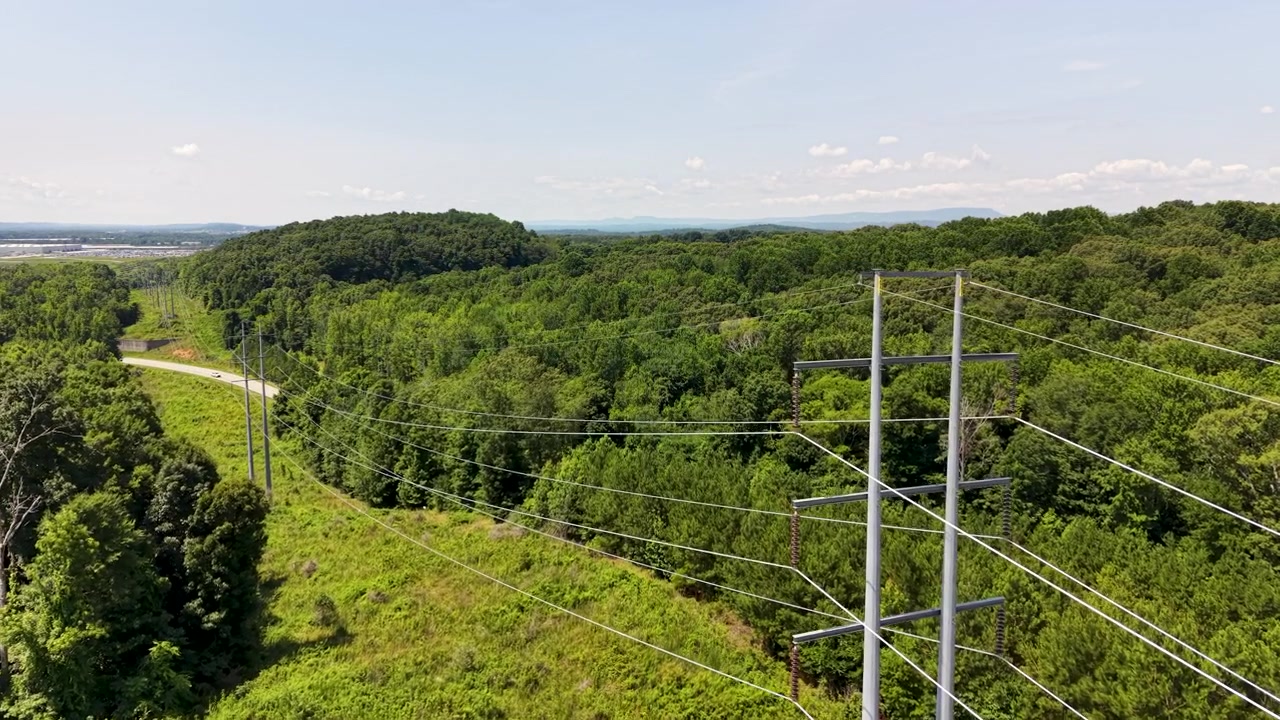 High-voltage transmission corridor near Chattanooga, Tennessee, United States, revealing steel monopoles, overhead conductors, deciduous forest, rolling hills and utility easement, drone forward flyov