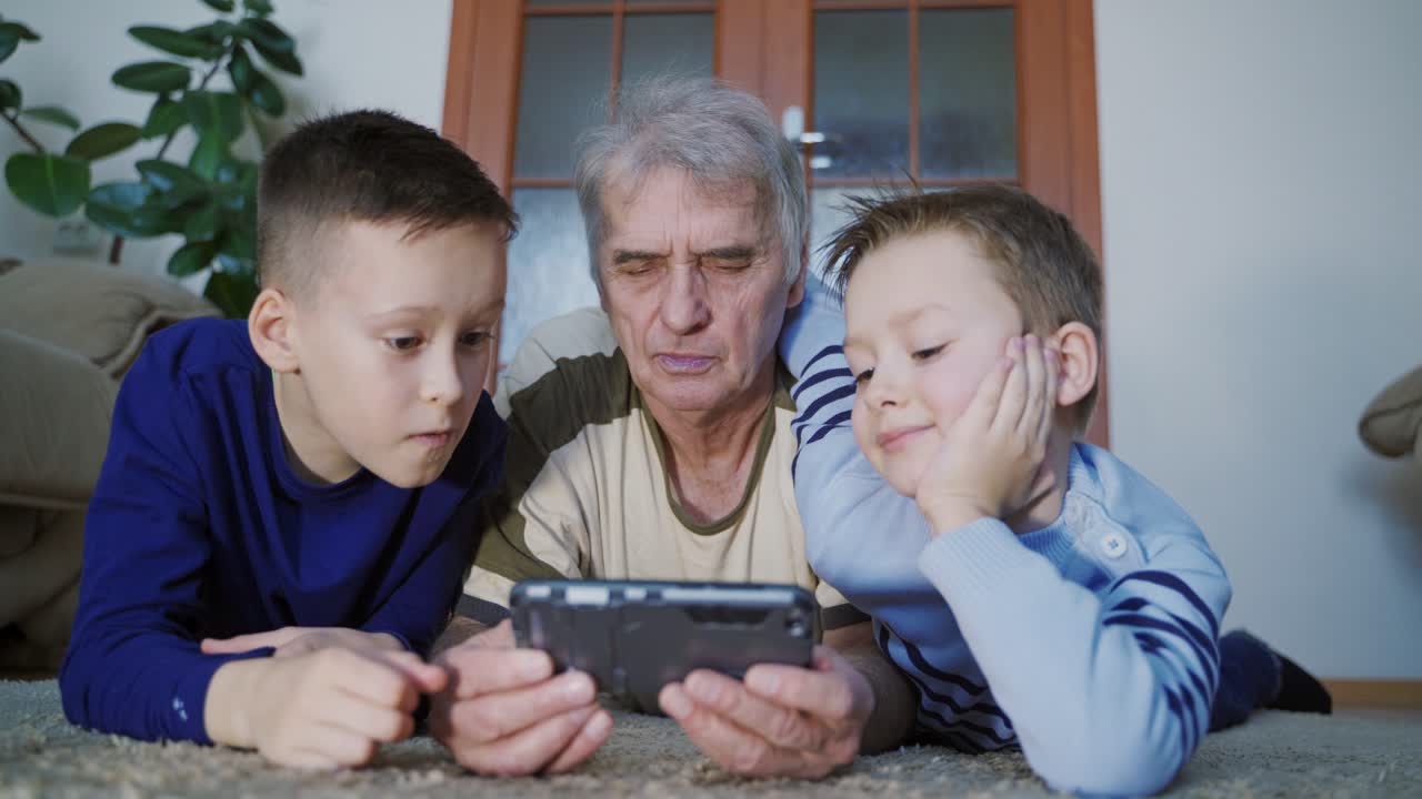 Family spending time together. Funny grandfather and grandsons using mobile phone
