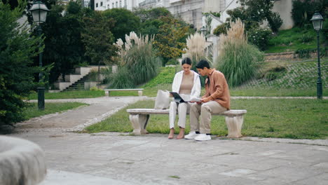 college students learning tablet on bench vertically. couple working green park