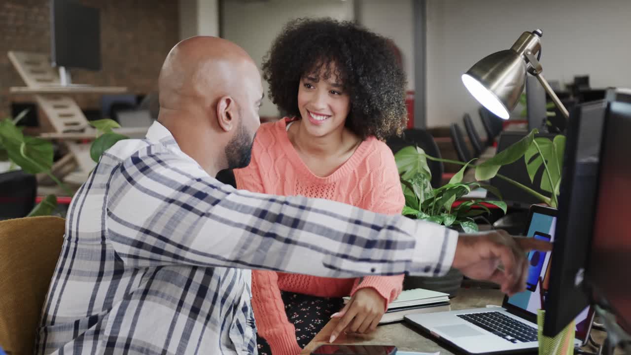 Two happy diverse creative colleagues in discussion at computer in casual office, slow motion