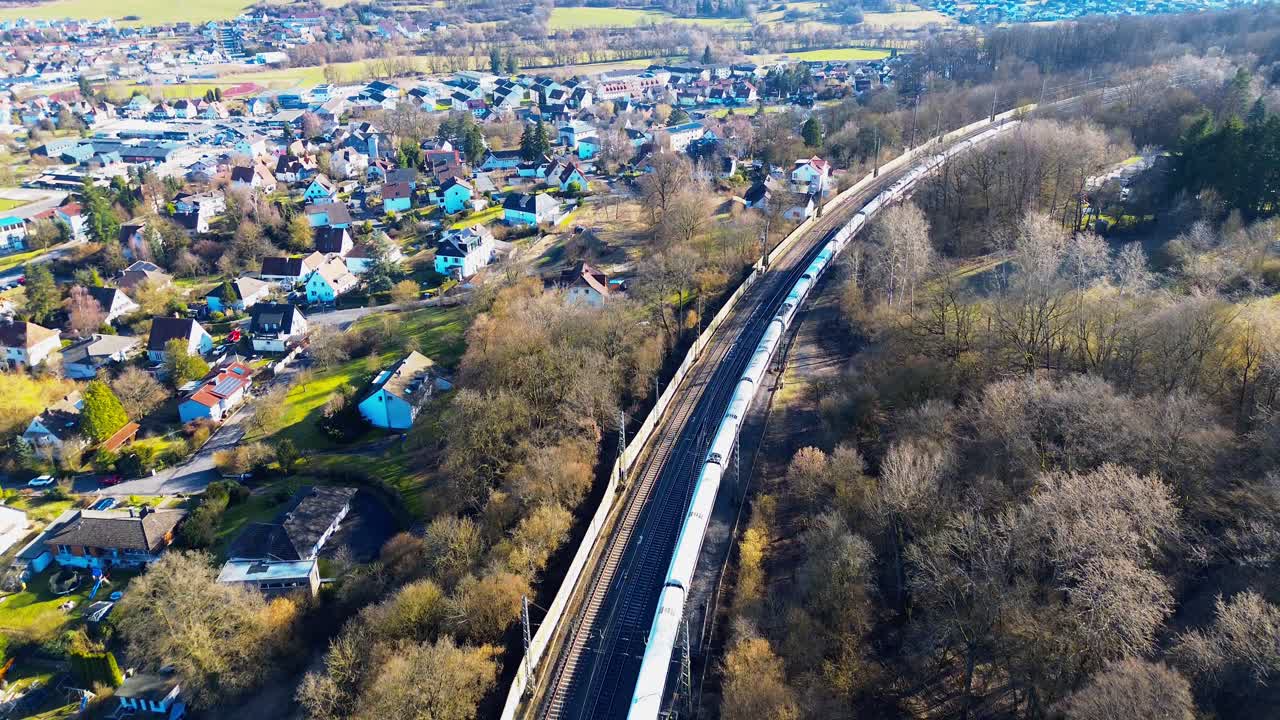 Almanya'da kırsal bir kasaba ve orman boyunca seyahat eden yolcu treninin havadan drone görüntüsü.