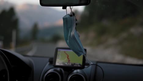 face mask hanging on drivers rear mirror while car moving on road covid-19 virus pandemic outbreak, detail slow motion