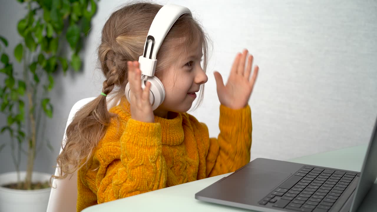 온라인 학습,  헤드폰을 입은 작은 금발 소녀는 노트북에서 배우고, 음악을 듣고 춤을 추고