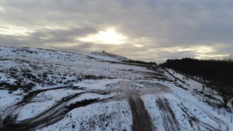 Schneebedeckter-Rivington-Pike-Tower-Winterhügel-Aus-Der-Luft-Steigende-Ansicht-Leute,-Die-Bei-Sonnenaufgang-Bergab-Rodeln