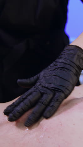 cosmetologist covers the male client's chest with special cream. care about skin after laser epilation procedure. vertical video