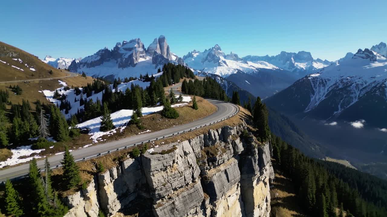 Telecamera in movimento che rivela una strada di montagna tortuosa che costeggia una scogliera calcarea su un passo alpino, mostrando le cime.