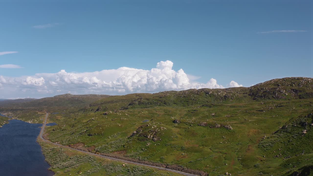 Norwegian landscape with green hills, road, and scenic blue skies, aerial view