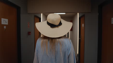 woman in a hat walking down a hotel hallway