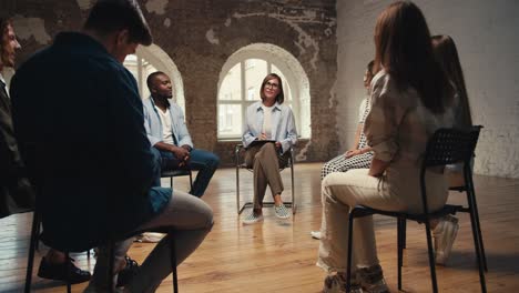 a girl psychologist with a bob haircut and glasses thanks the group therapy participants for their presence and the participants get up from their chairs and leave